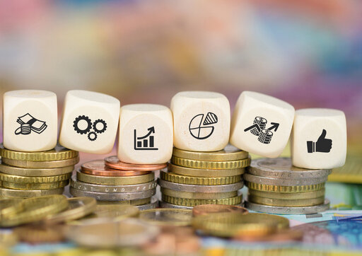 Das Bild zeigt mehrere Stapel Münzen, auf denen sich Würfel befinden. Auf einem großen Würfel steht dsa Wort "Weiterbildung", danach folgen sechs kleinere Würfel mit Symbolbilder, beispielsweise ein Daumen, der nach oben zeigt und ein Chart mit Aufwärtstrend.