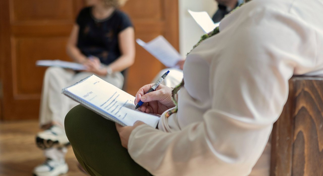 Ein Mensch in einem Stuhlkreis hält einen Notizblock in der Hand und schreibt