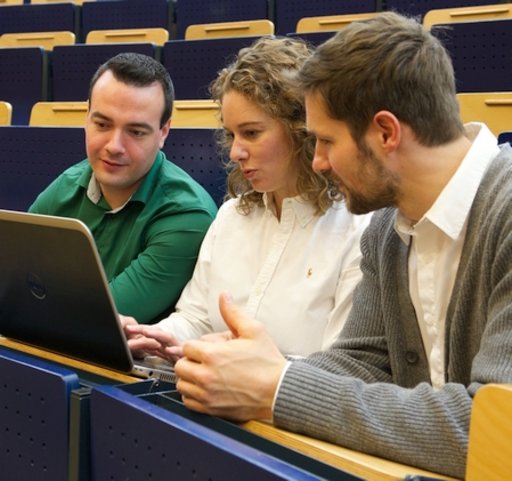 Drei Studierende sitzen im Hörsaal und schauen gemeinsam auf einen Laptop.
