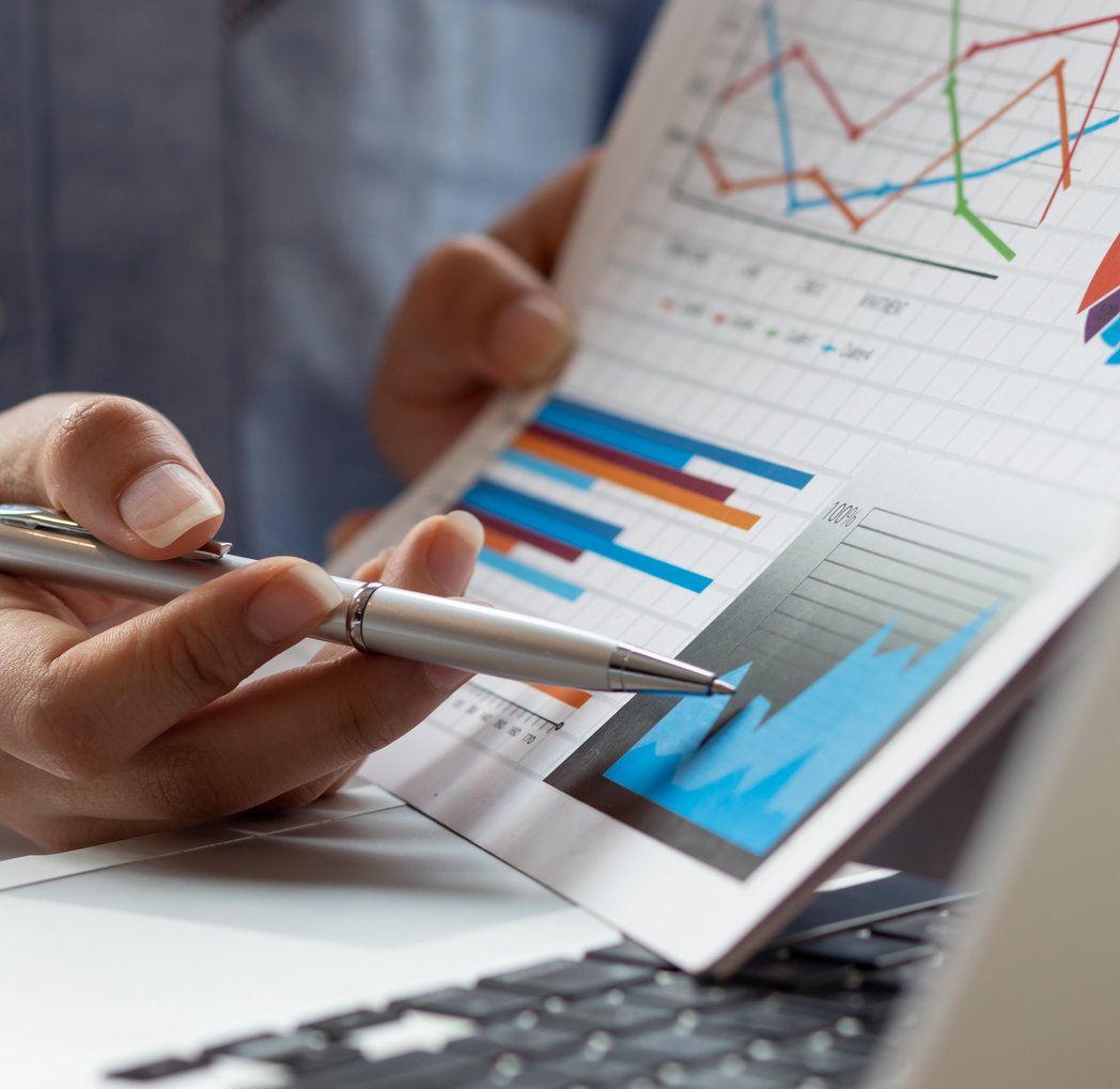 Ein Mann sitzt an einem Tisch und zeigt mit einem Stift auf Grafiken auf einem Blatt Papier. Das Gesicht ist nicht zu sehen. 